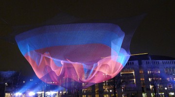 A hanging net being colourful lit in front of the Muziektheater