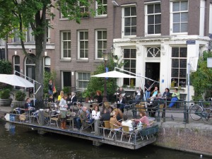 People sitting on the terrace that hangs over the water of the canal