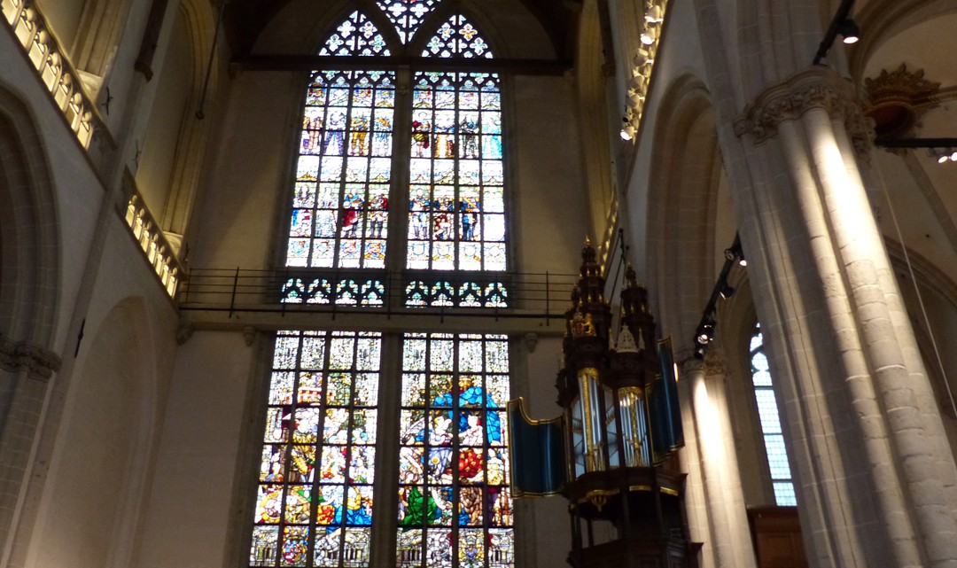 An enormous stained glass window with the small dark wooden organ to the right