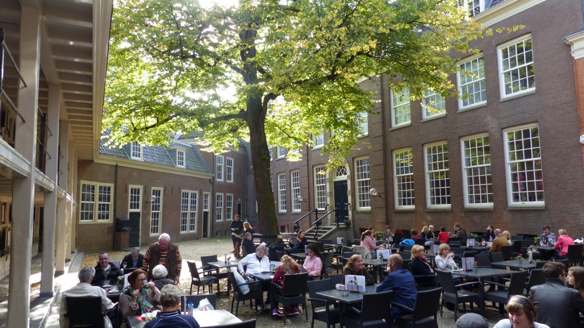 A busy terrace in the shade of a large tree on a sunny day