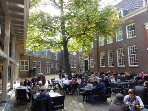 A busy terrace in the shade of a large tree on a sunny day