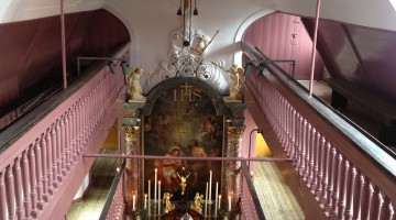 A view from the second balcony, with pink balustrade, into the small, narrow church towards the altar