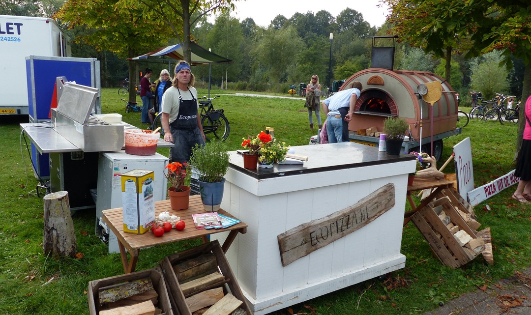 A basic counter on the grass. Behind it a mobile wood-fuelled pizza oven