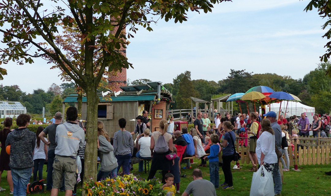 A crowd watching an acrobat juggling in front of a wooden caravan with solar panels