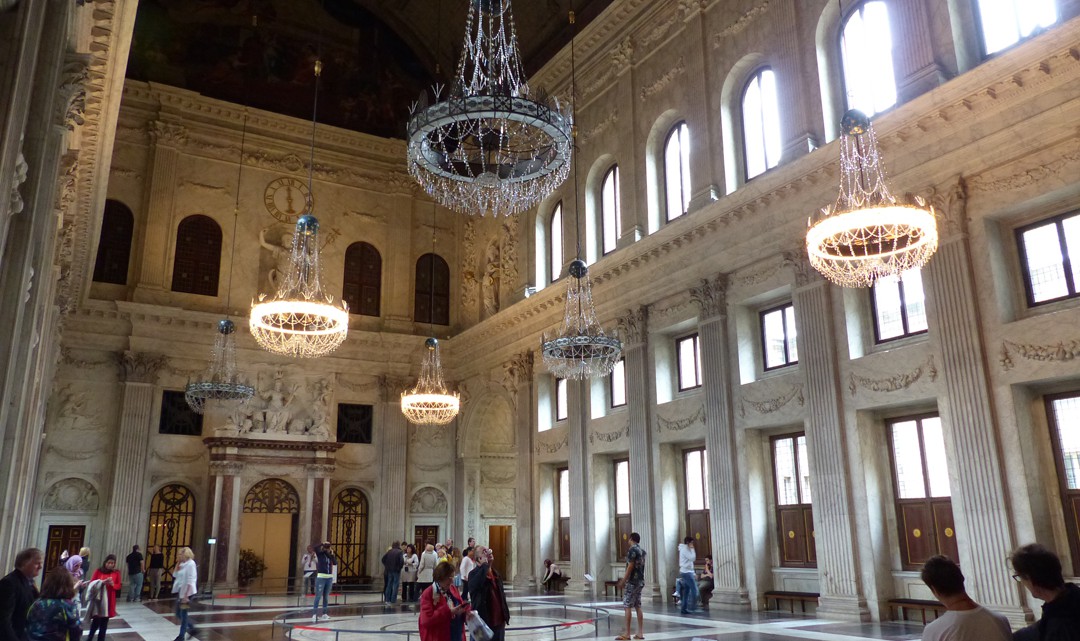 An enormous hall with wooden vault ceiling, marble walls and floor and six enormous chandeliers that look quite small