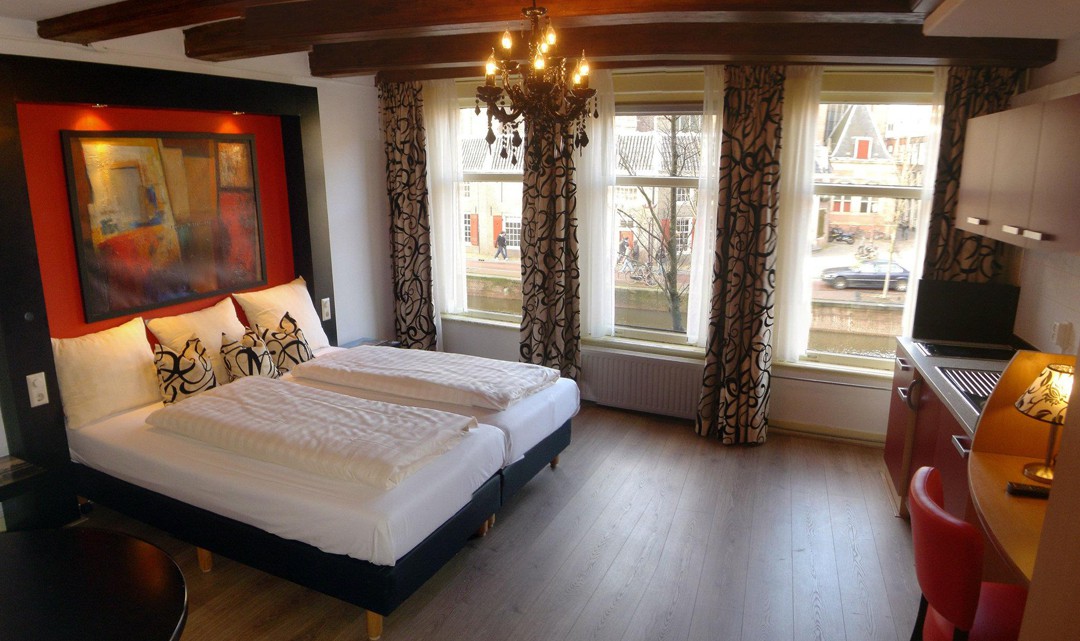 A classy looking bedroom with wooden floor, a chandelier, expose ceiling beams and a view on the canal